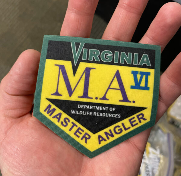 A photo of a hand holding an iron-on patch with Virginia Master Angler VI written on it.