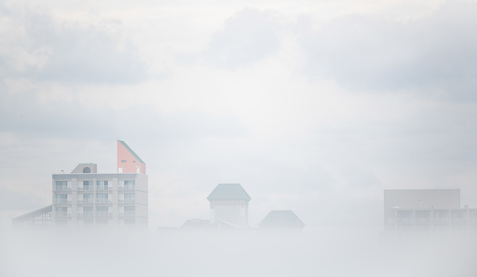 A photo of fog with just the tops of buildings popping through the top of the mist.