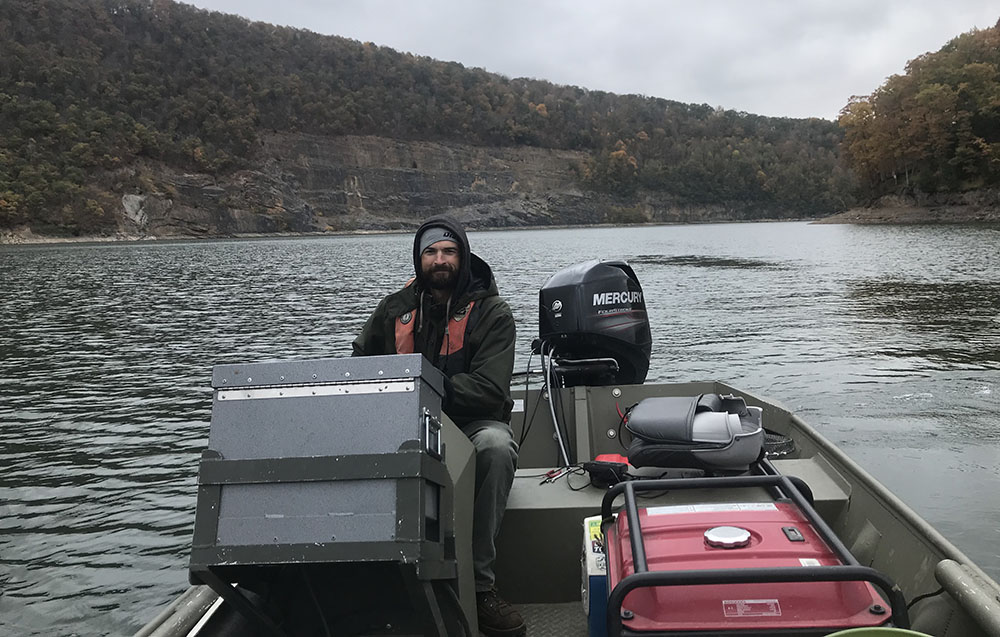 An image of a biologist in a boat at the steering apparatus leading a tour of Lake Moomaw