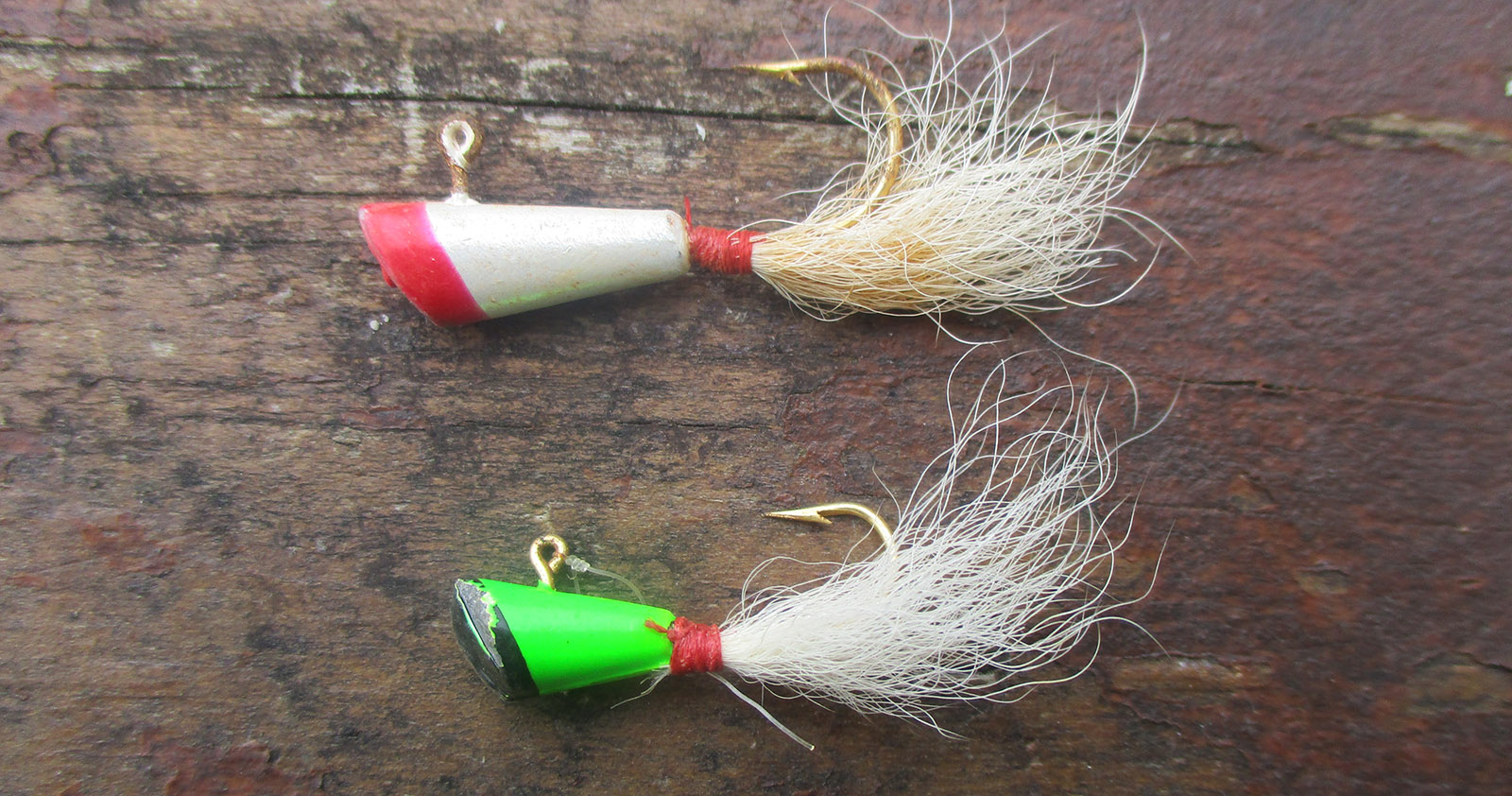 Two fishing lures, one read and white, one green and black, both simple with fuzzy tails.