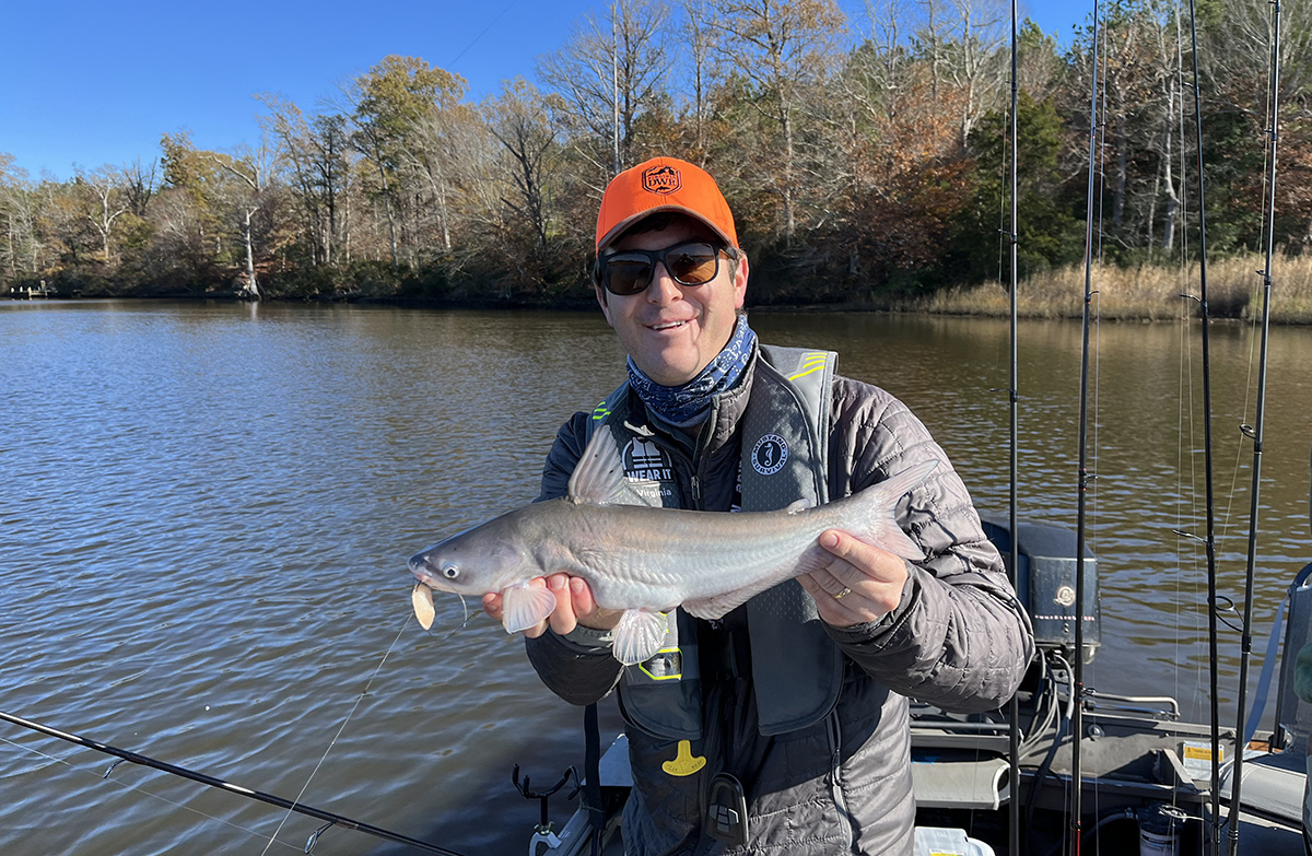 An image of the Angling education coordinator holding a large blue catfish in front of a lake