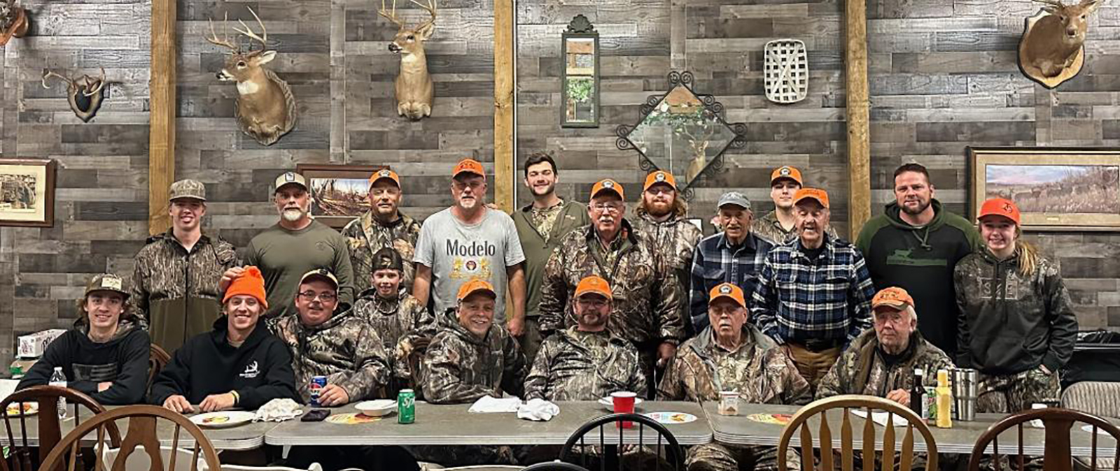 A photo of 19 men all dressed in camouflage, sitting and standing behind a long table.