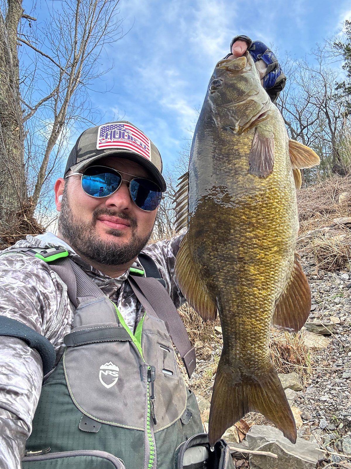 A photo of a man in a life jacket holding up a large smallmouth bass.