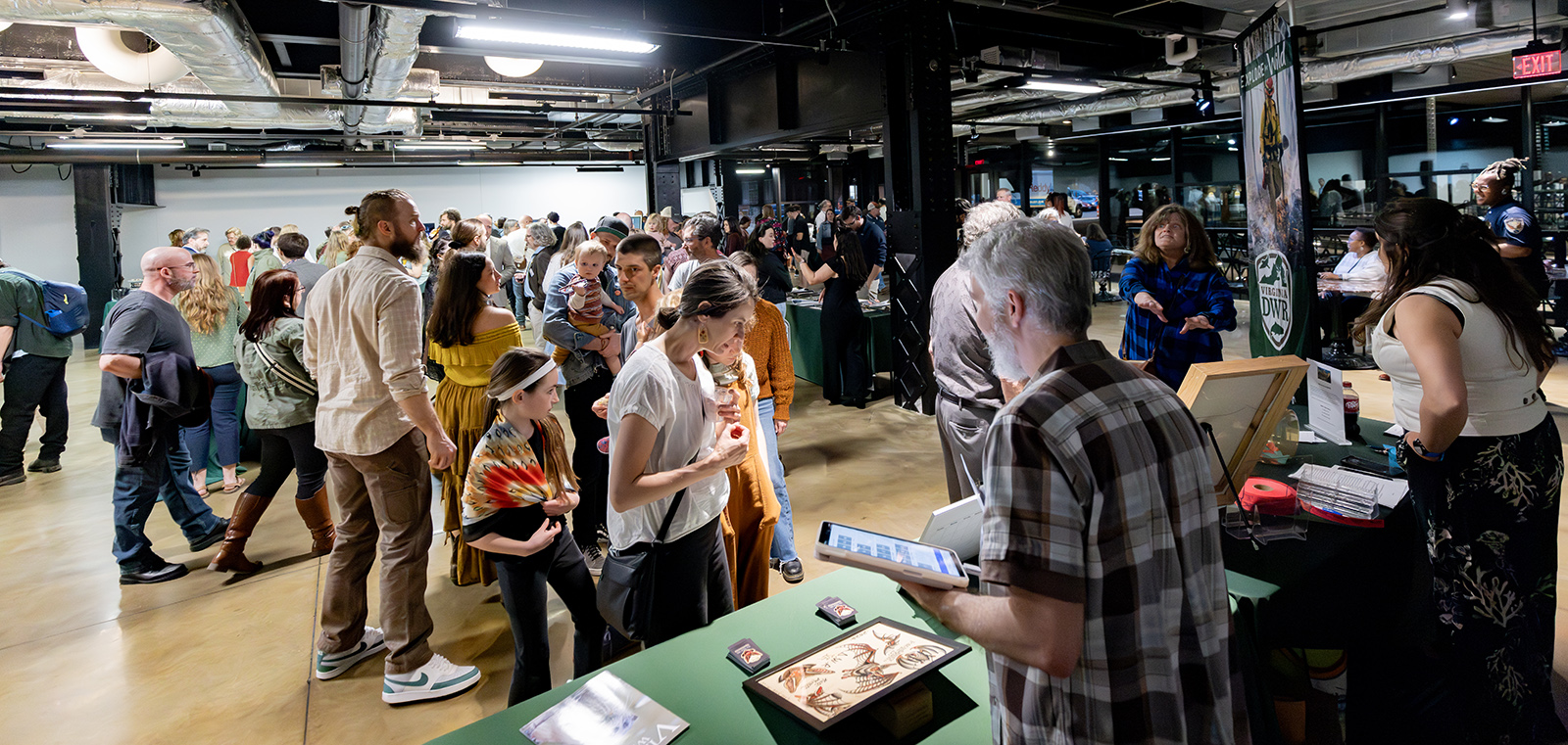 A photo of a line of people in a large room, waiting to buy items placed on a table.