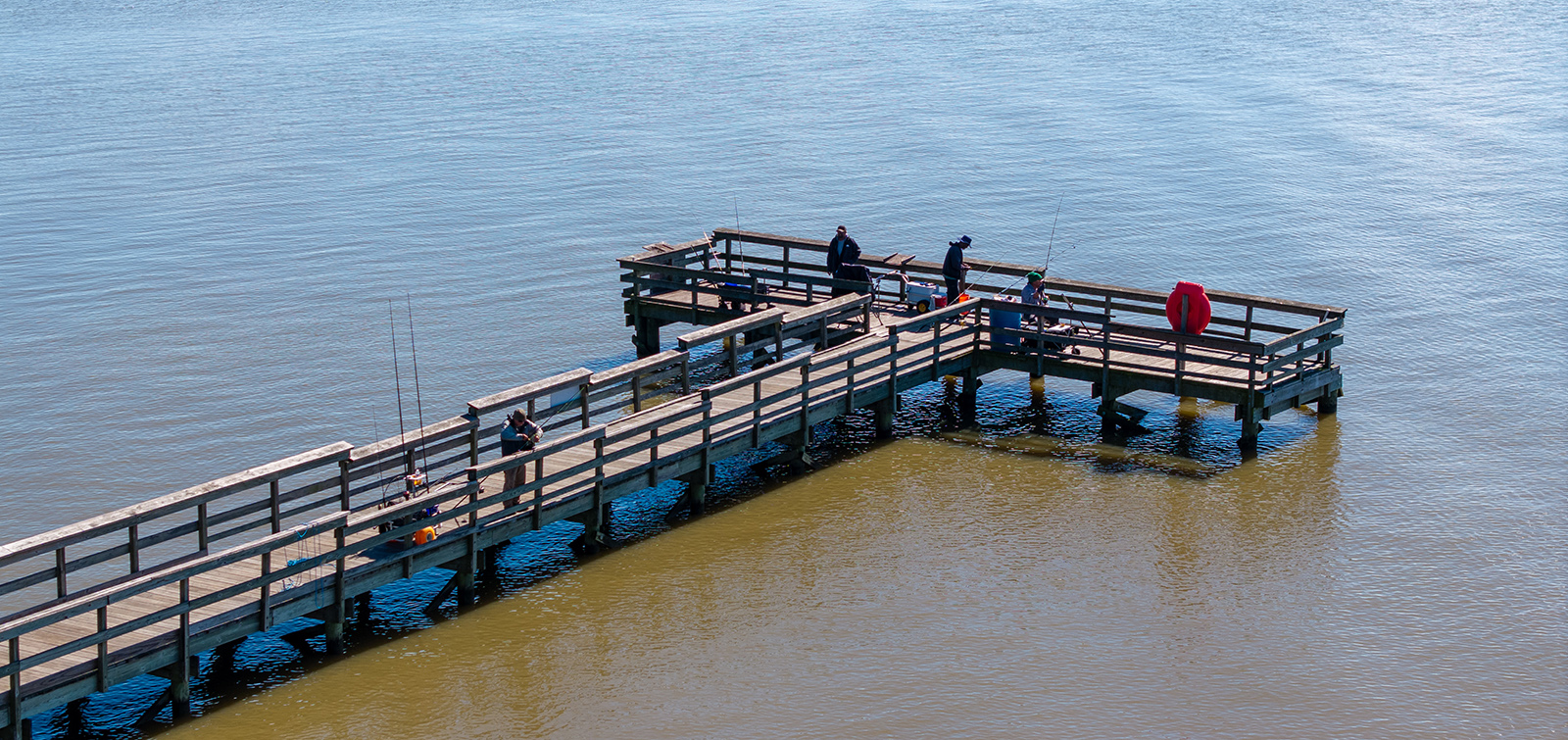 An aerial photo of a large T-shaped fishing pier in the water of a river.