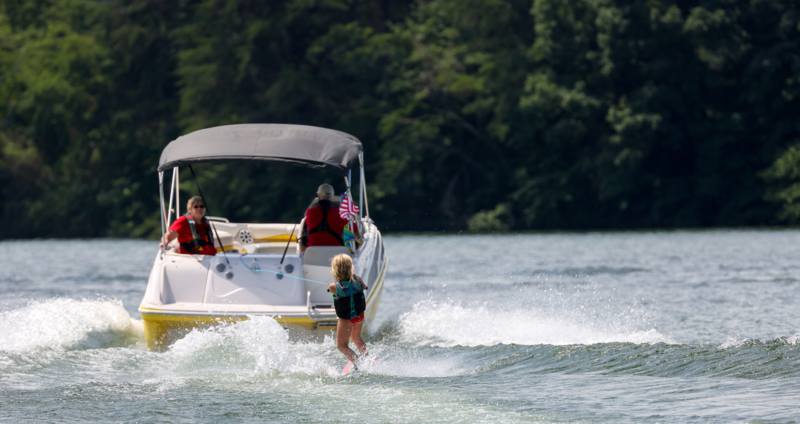 A photo from behind of a boat pulling a young waterskier.