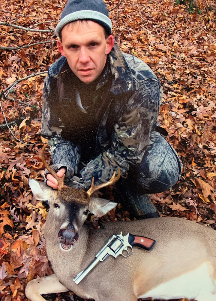 An image of a hunter and a deer he had shot with a handgun