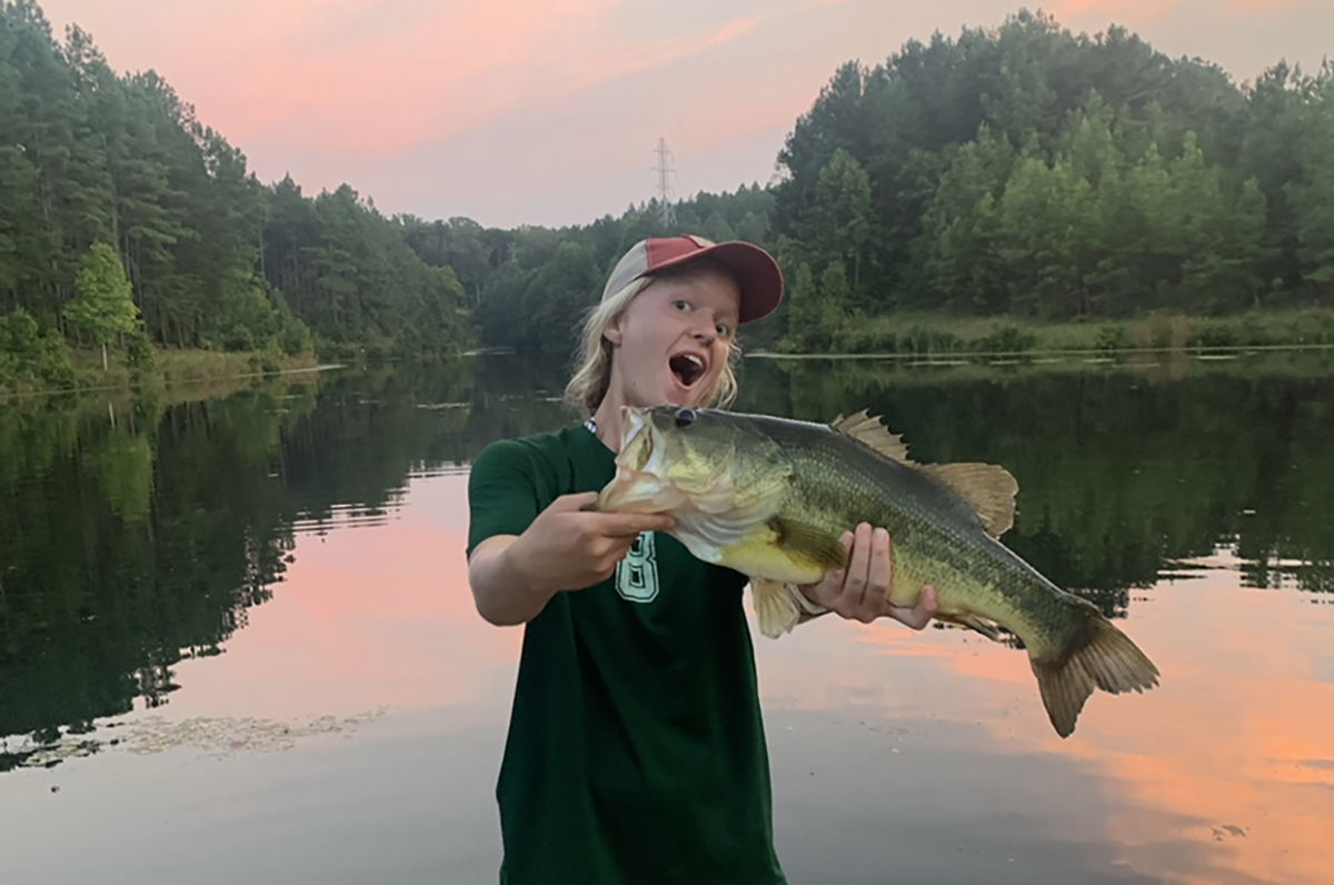 An image of Annie holding a largemouth bass in front of a lake