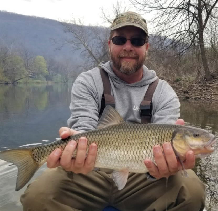 A photo of a man holding a large fallfish with a river in the background.