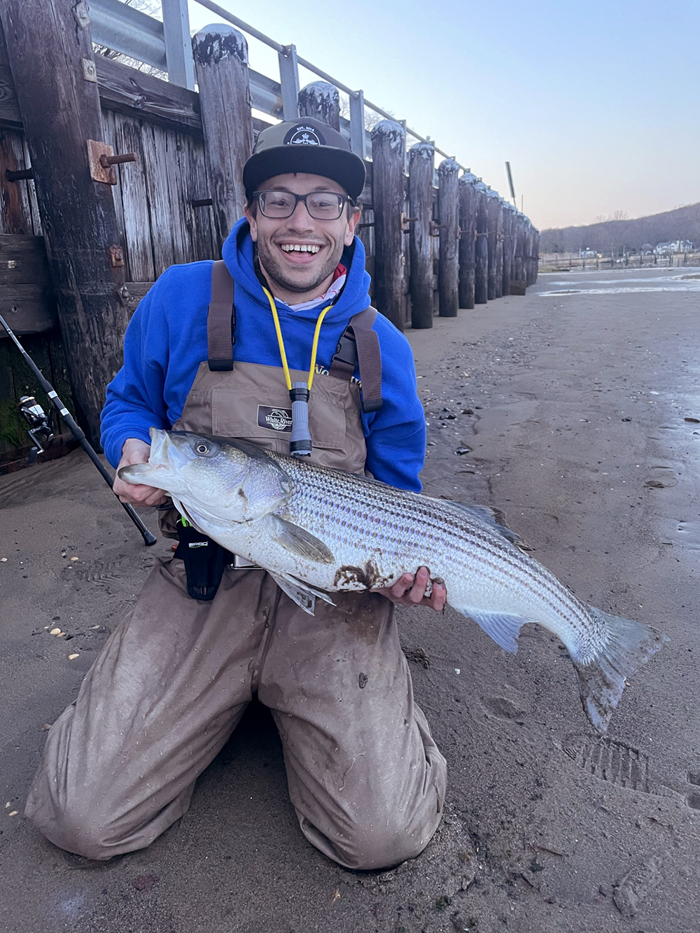 An image of Josh McGilly on a beach holding a large striped bass