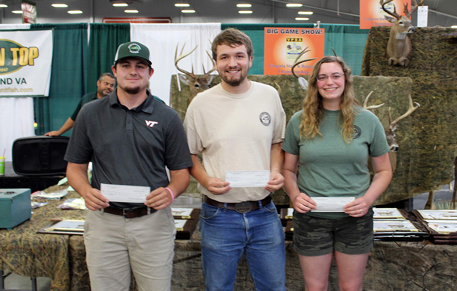 A photo of three young people, two men and a woman, holding checks and smiling.