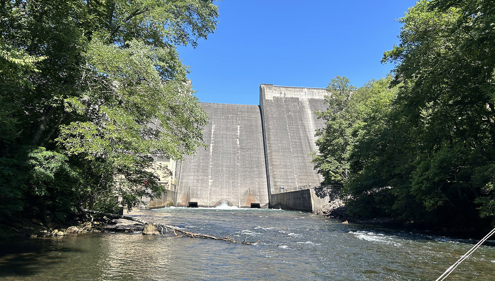 A photo of a tall, concrete dam taken from the river below it.