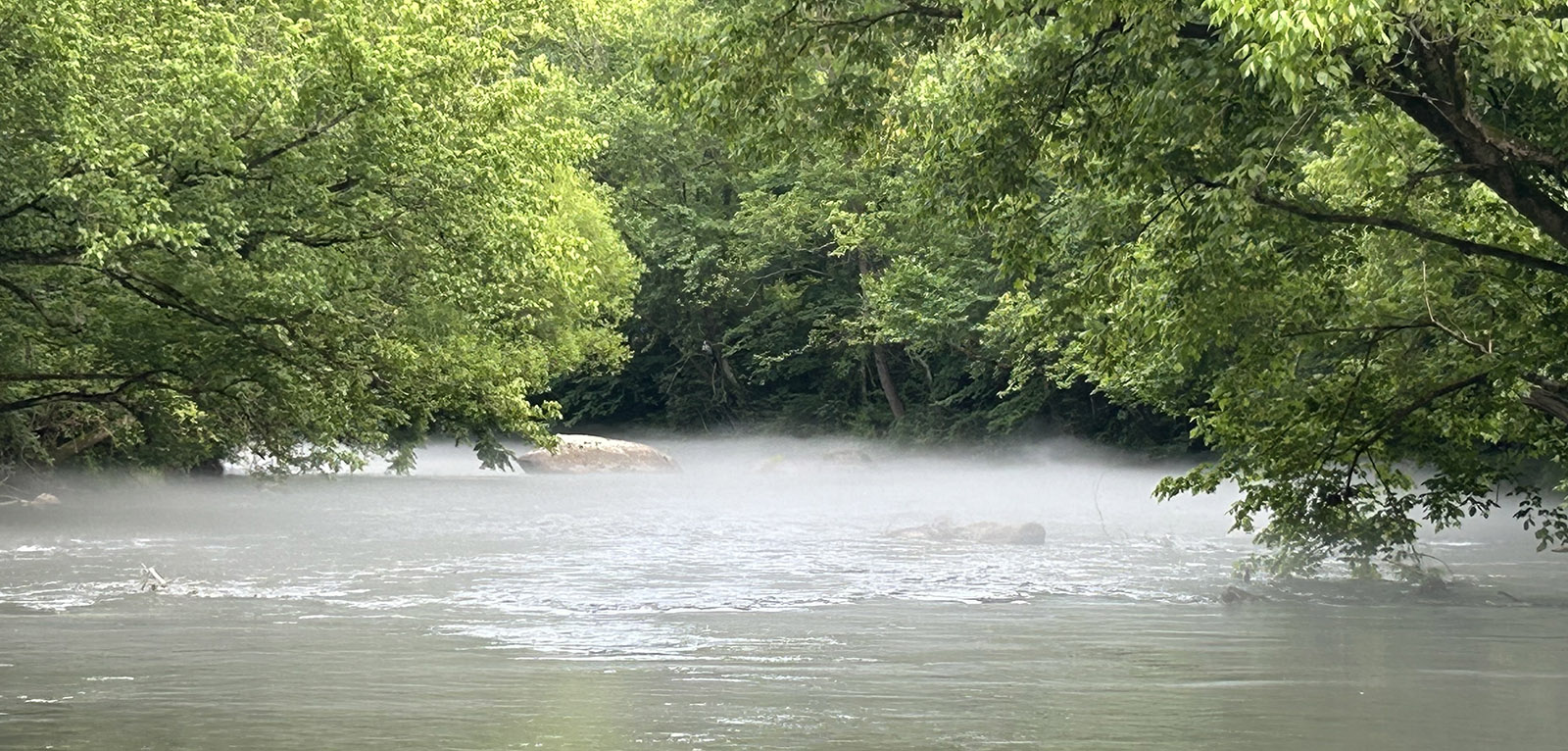 A photo of a river with a light fog lifting off the surface of the water.