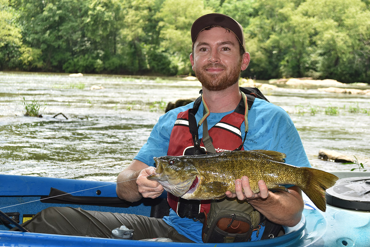 An image of a man in a blue boat holding a smallmouth bass