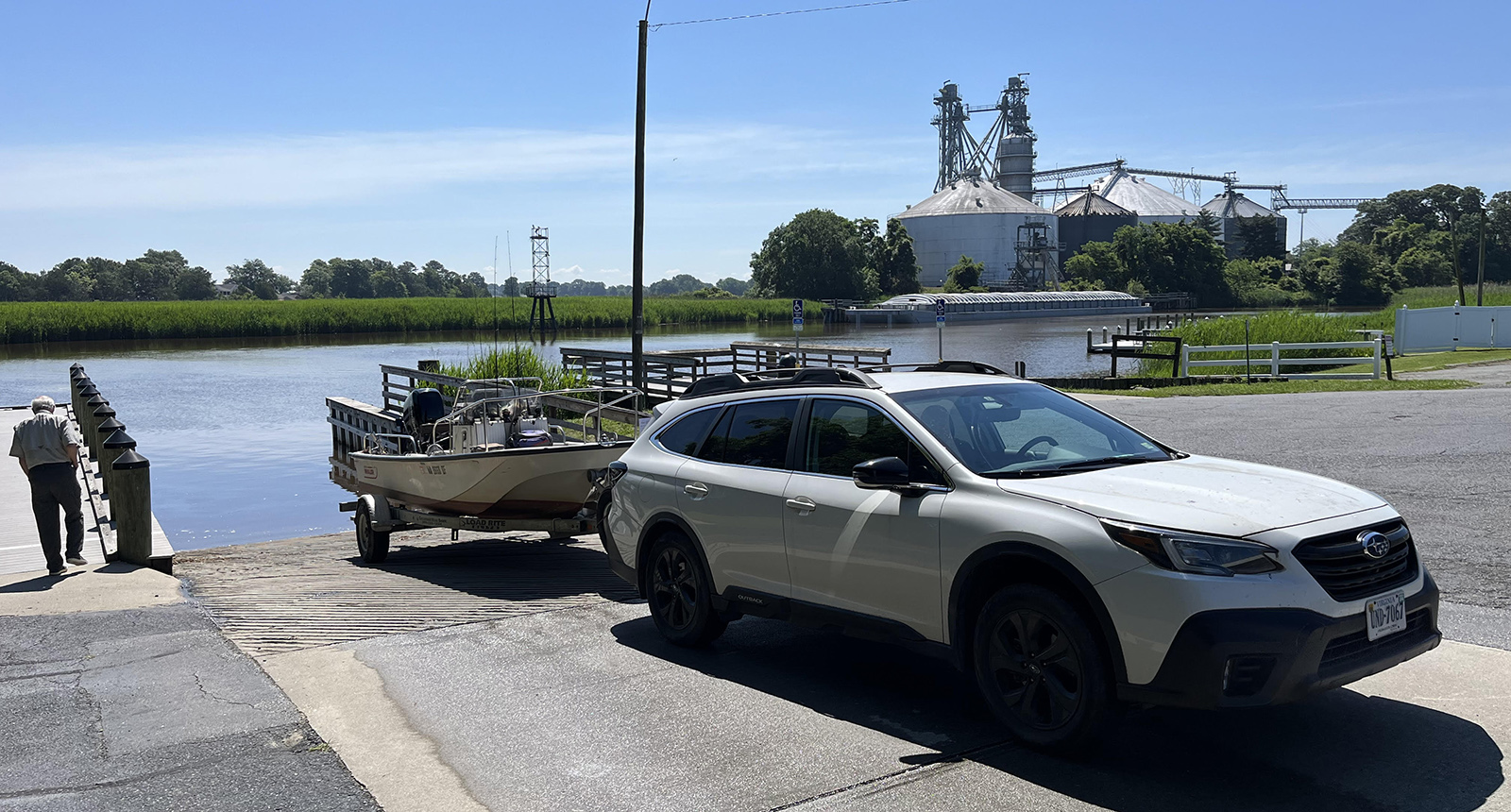 A photo of a car pulling a small motor boat and about to back down a boat ramp incline to the river.