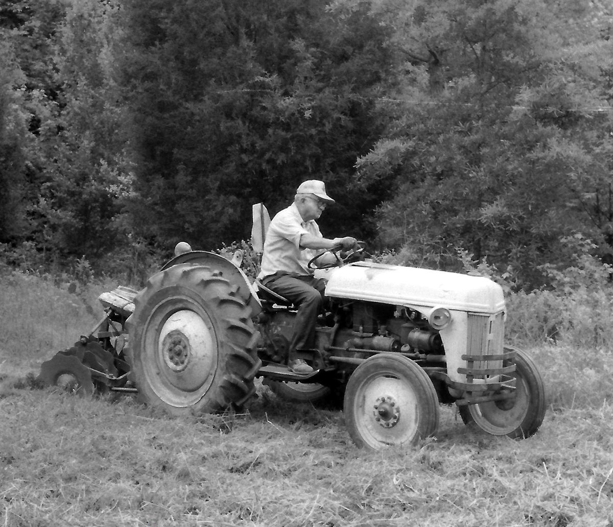 An black and white image of a man with a tractor tilling a field