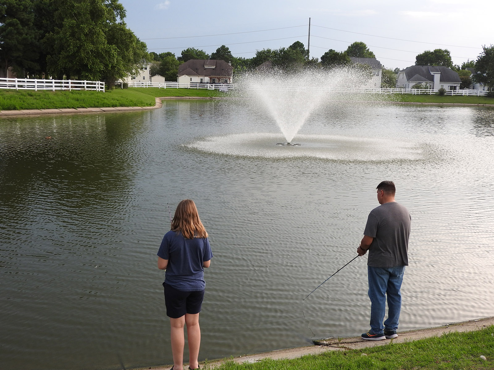An image of a man and girl standing on the banks of a lake fishing in a local retention pond