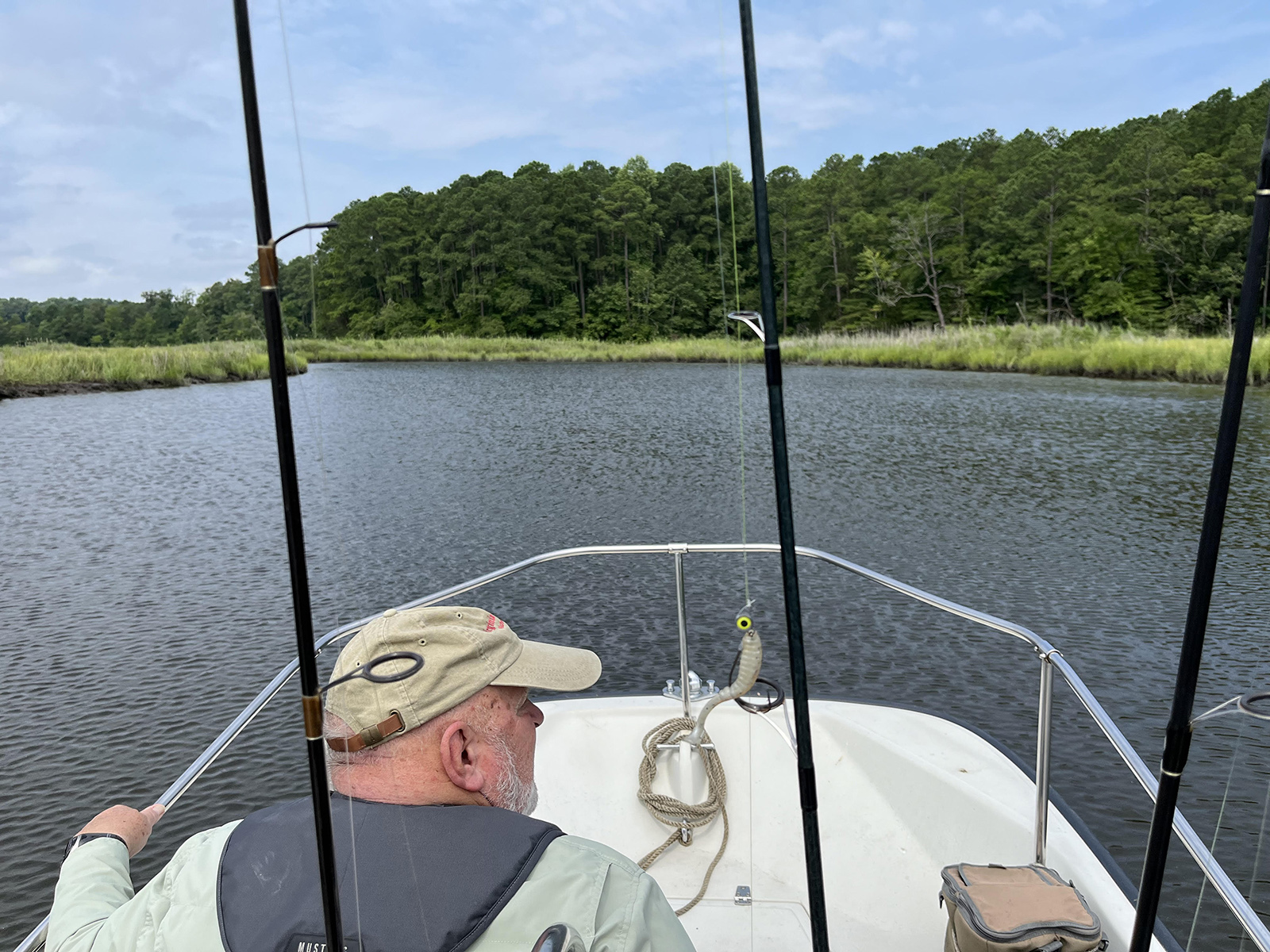 A photo of the bow of a boat with a man sitting on it heading into a narrower piece of water with marsh on the edges.