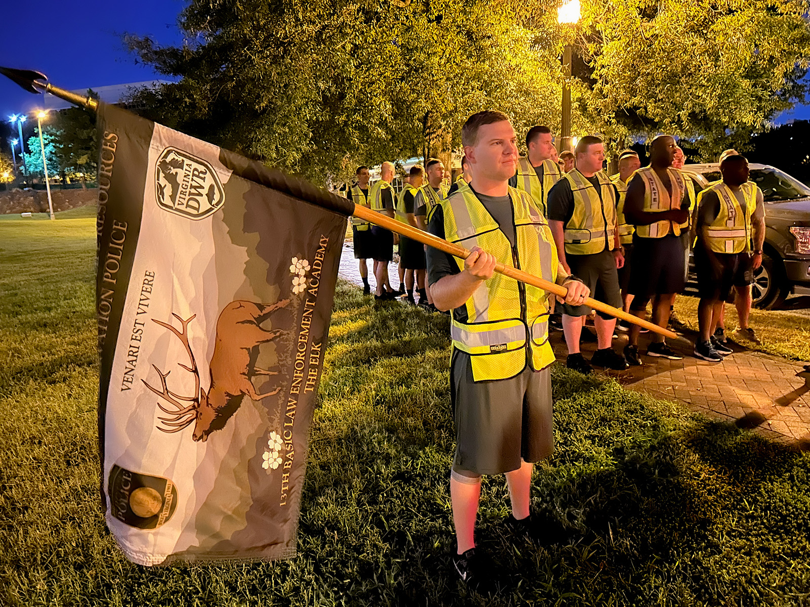 A photo taken in dawn light of a group of young men and women preparing to run. The man in front is holding a DWR flag with an elk on it.