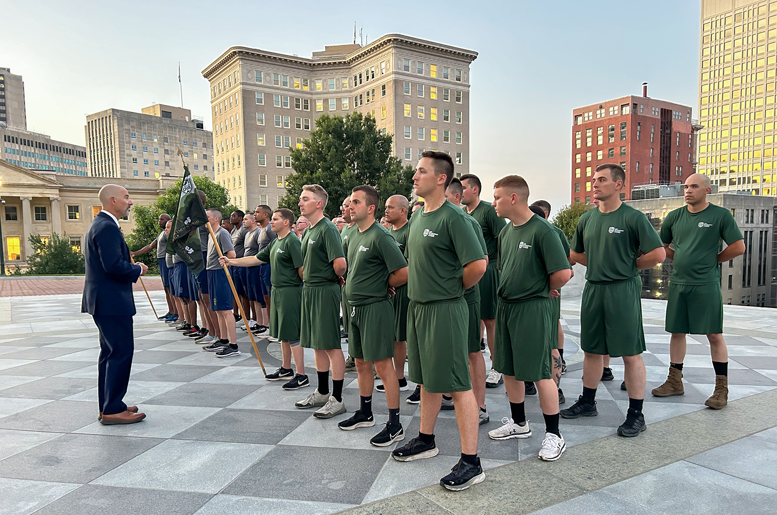 A group of young men and women standing at attention being addressed by a man in a suit while standing on the stairs of the Virginia Capitol building.