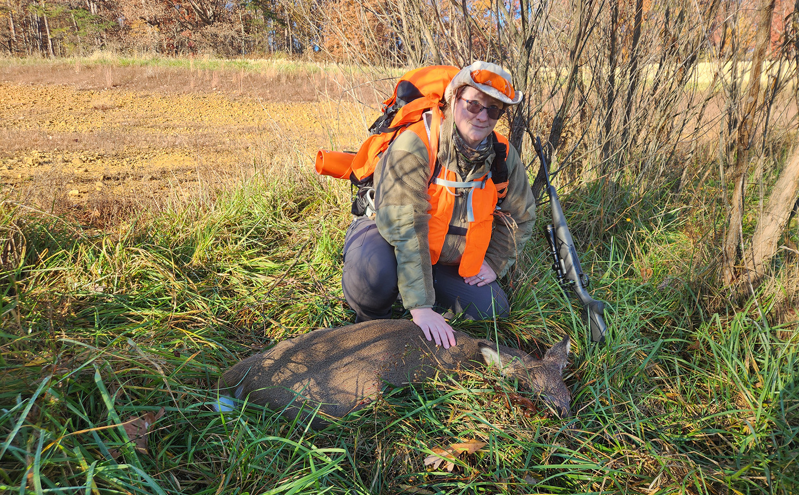 A photo of a woman kneeling beside a harvested doe deer.
