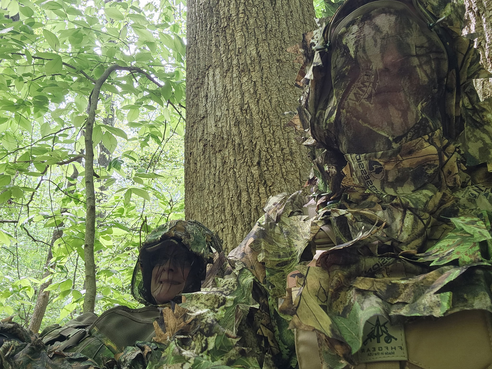A photo of two woman in the woods wearing camouflage and face screens.