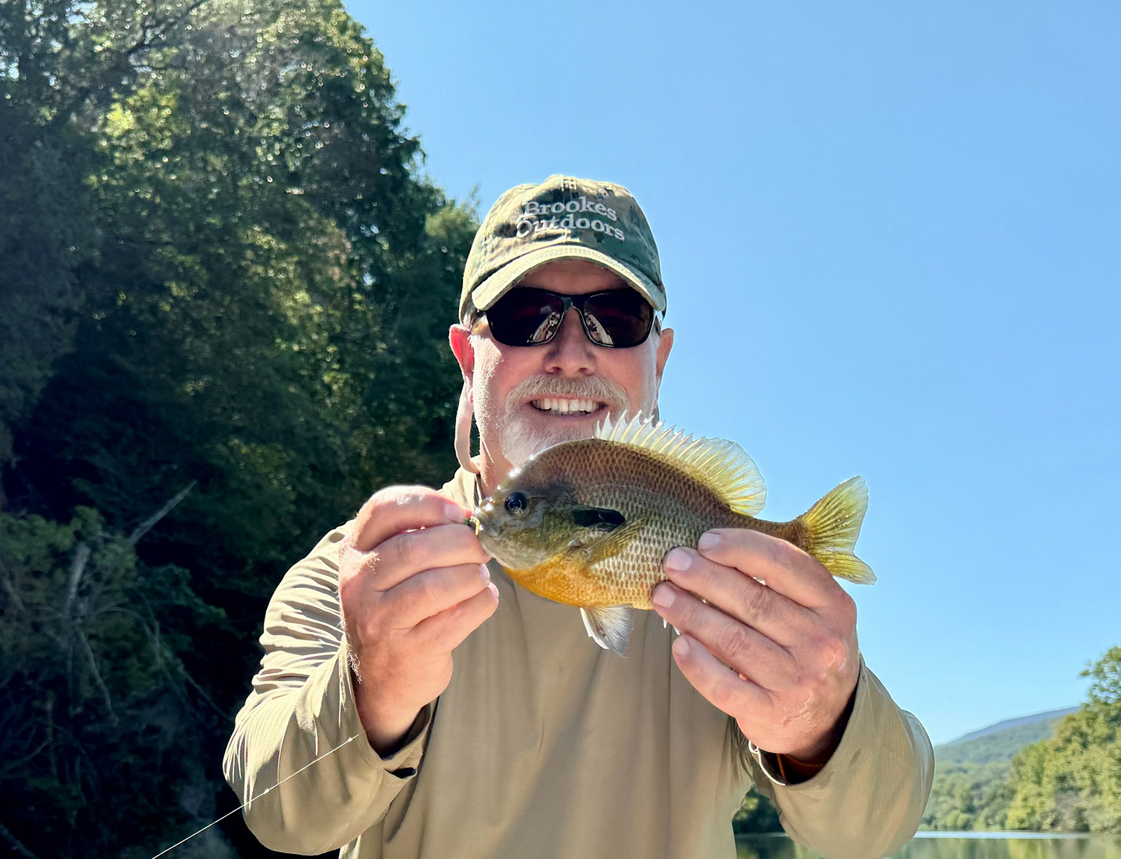 A photo of a man holding up a small fish and smiling.