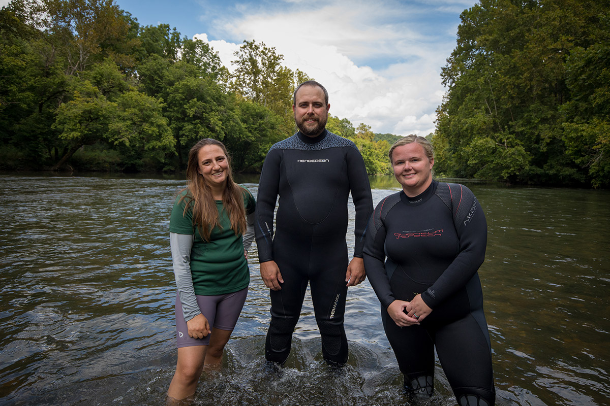 An image of a trio of people standing in a river posing for an image