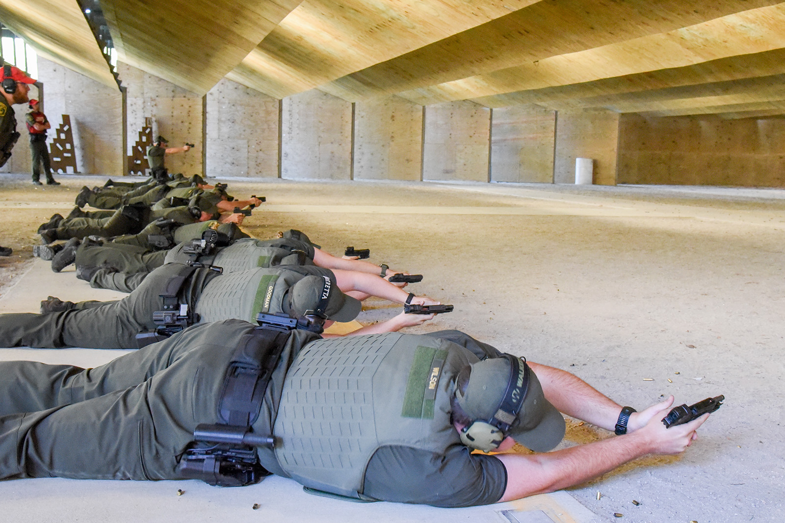 A photo of a line of men and women at a shooting range, lying on their sides and aiming pistols at targets.