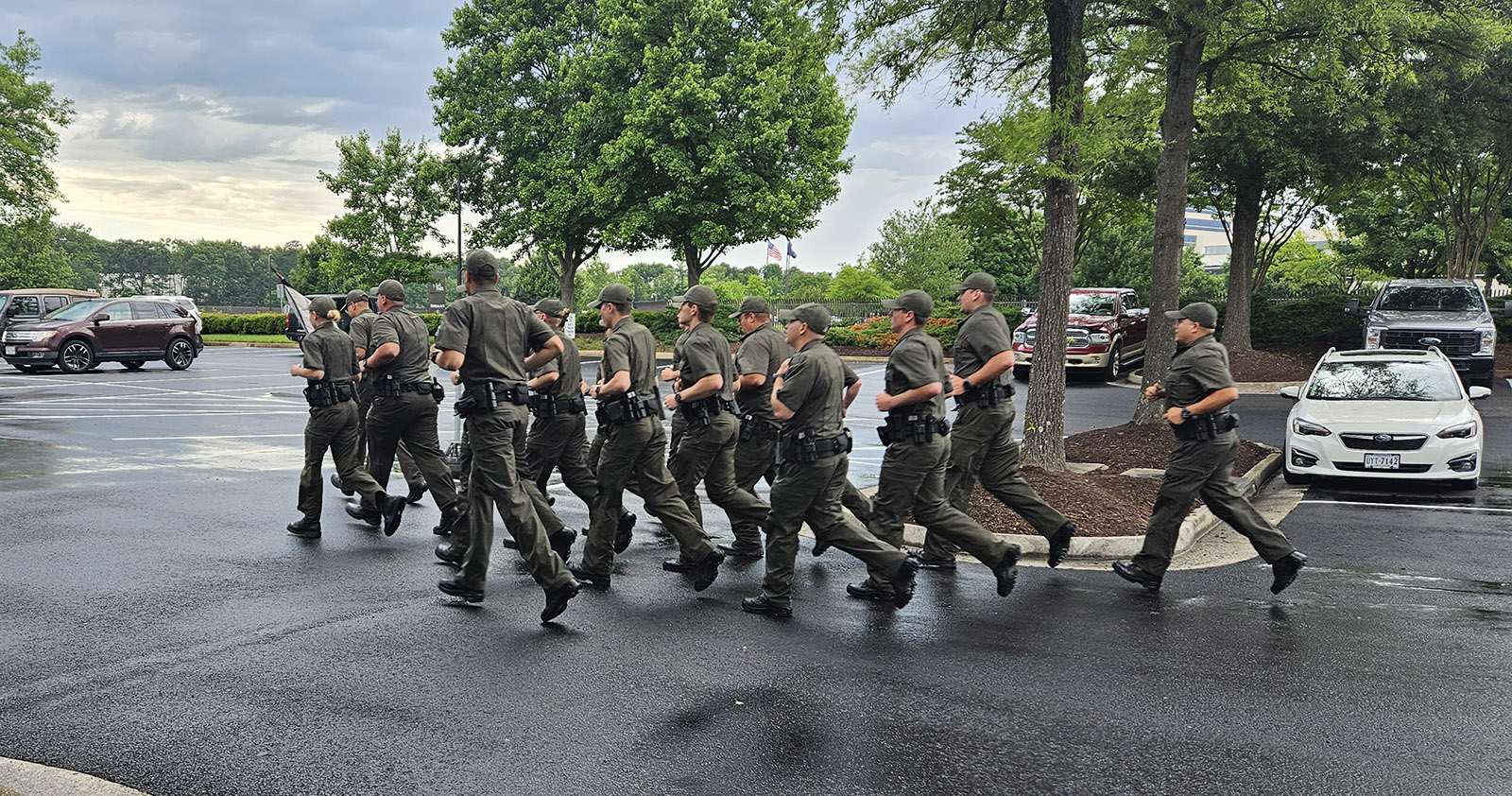 A photo of men and women in uniform running through a parking lot.