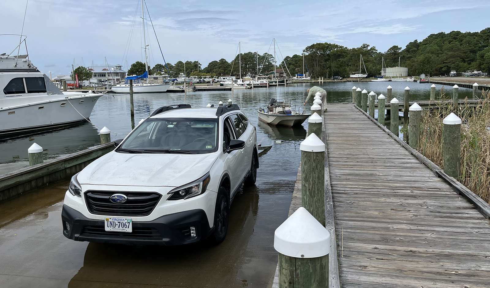 A photo of a white car parked on a boat ramp with a small skiff in the water.