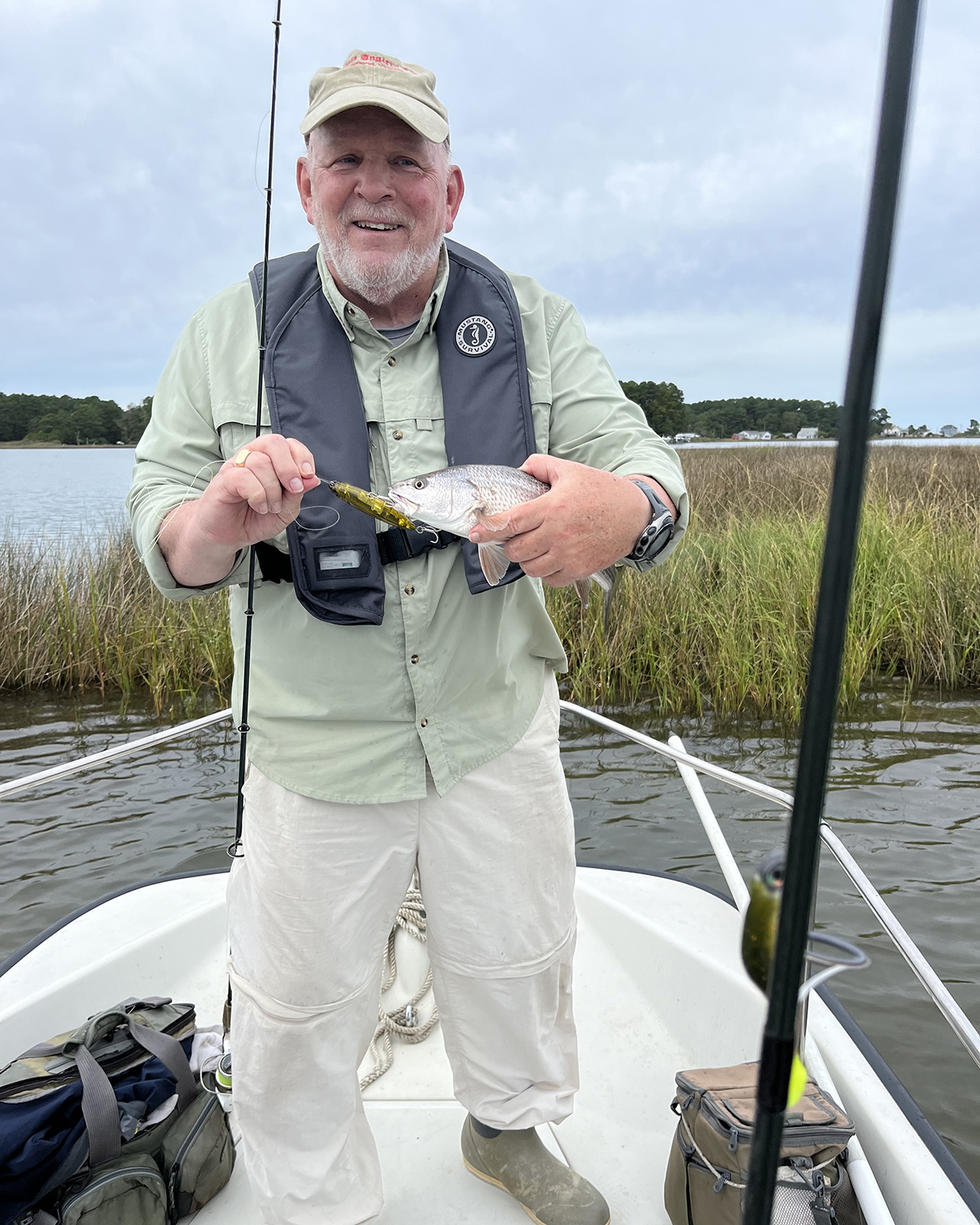 A man wearing a life jacket standing on the bow of a boat holding a fish and smiling.