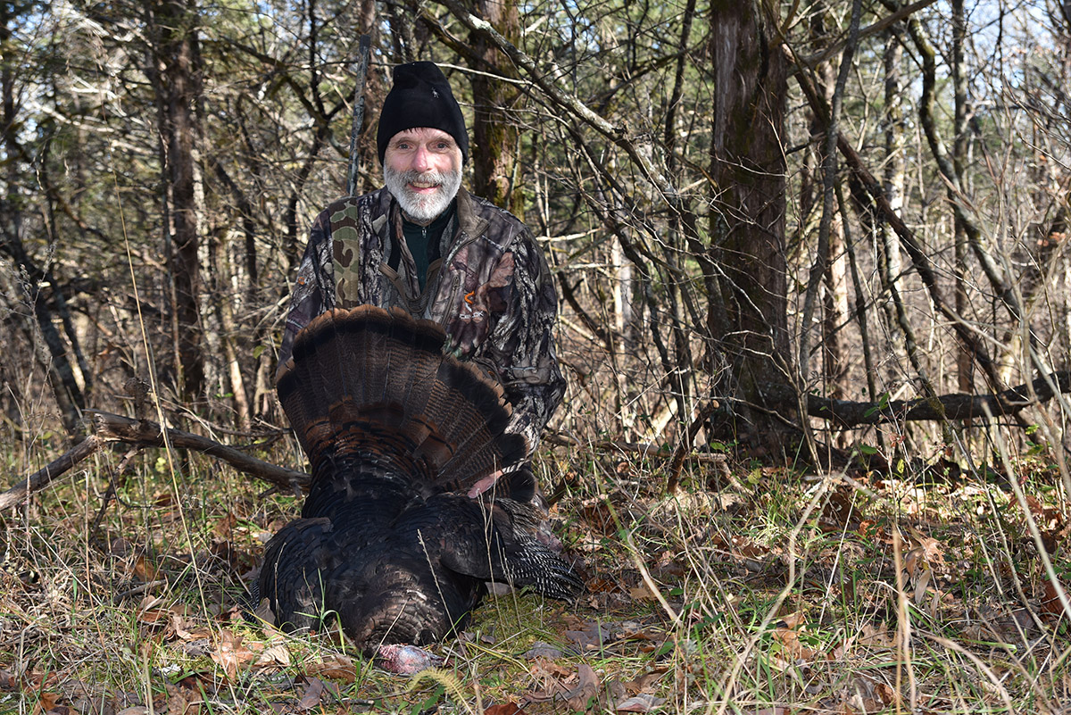 An image of a man in camouflage with a gun and a dead turkey which he had shot