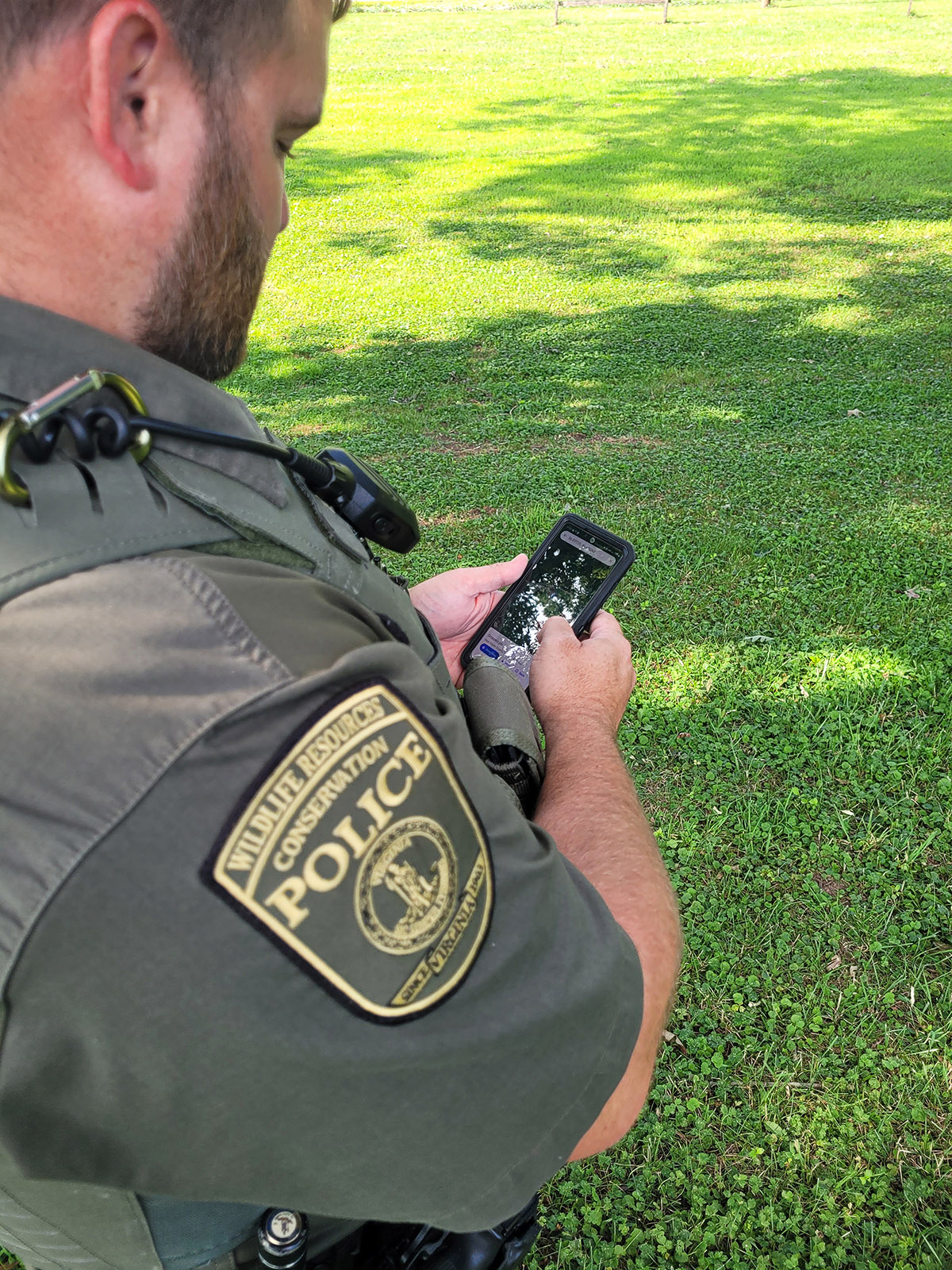 A photo of a Conservation Police Officer looking at a mobile phone.