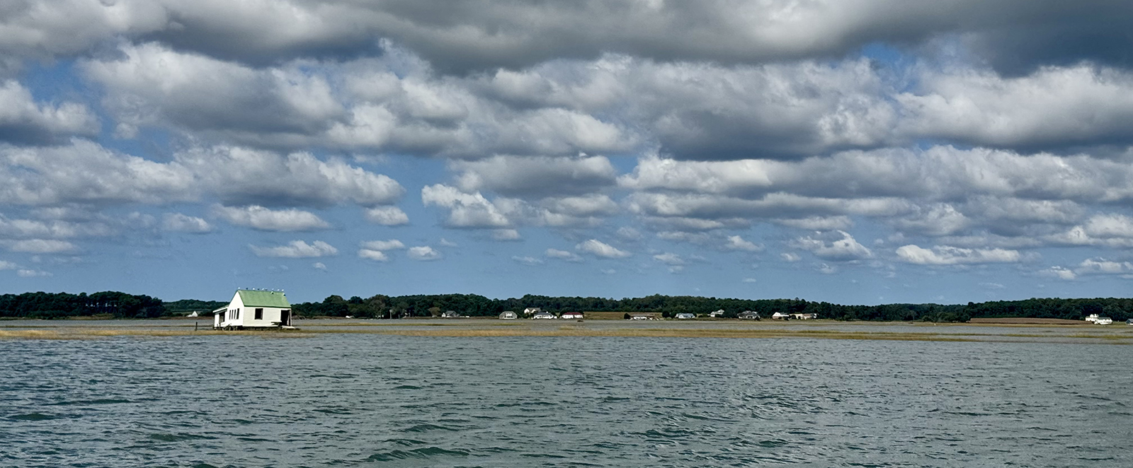 A landscape photo of a wide stretch of water with a small house in the background.