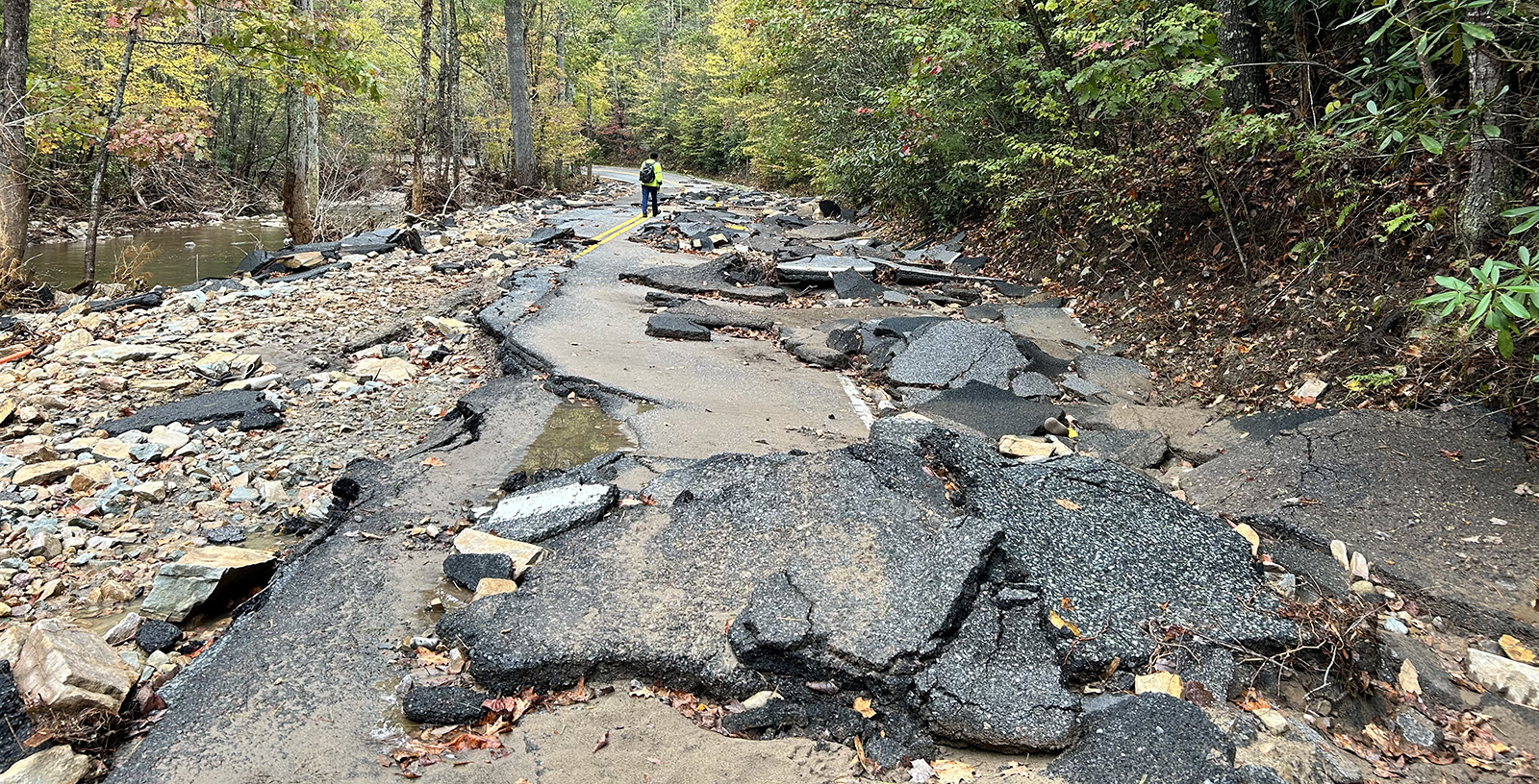 A photo of a destroyed road, with pieces of asphalt strewn around, next to a stream.