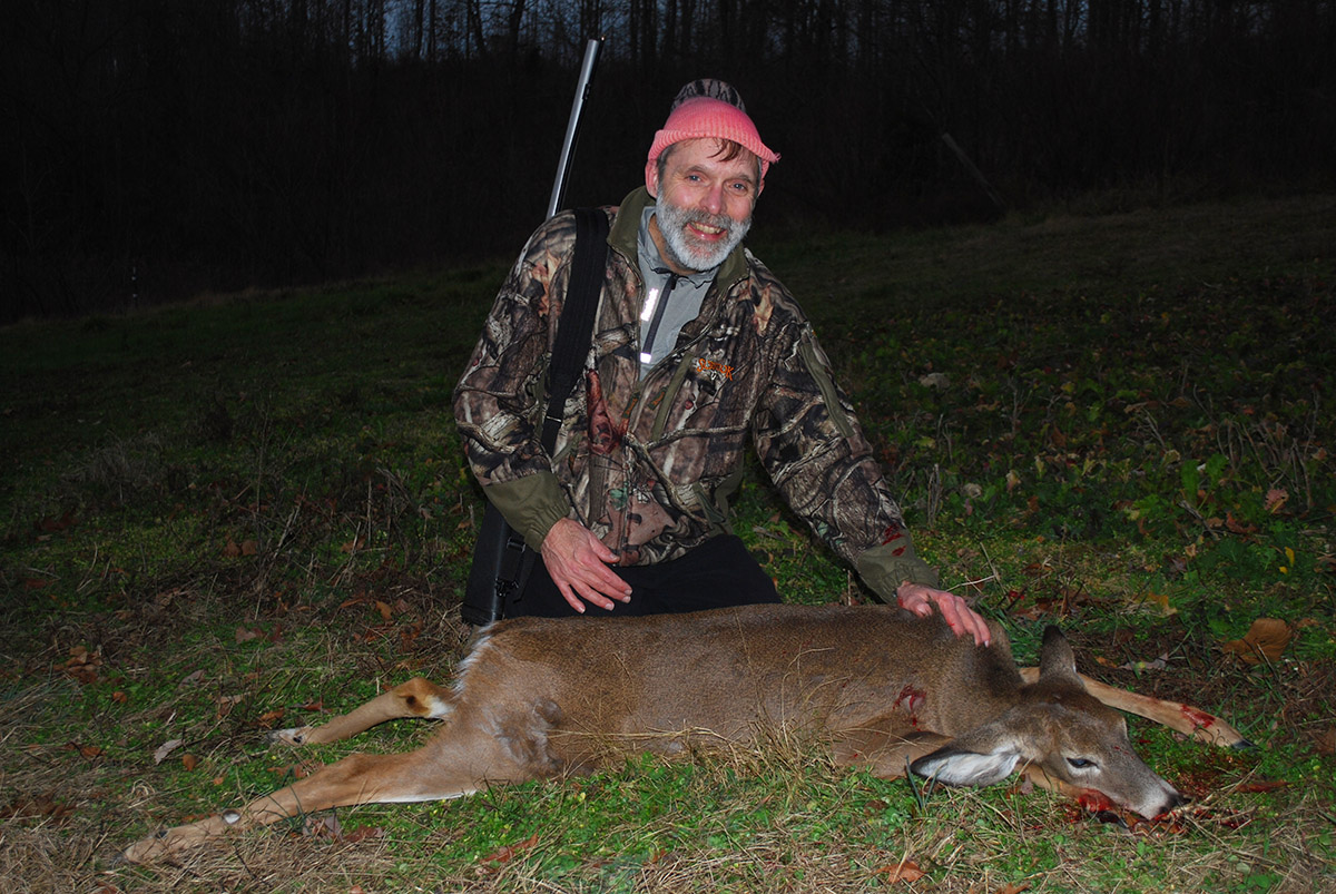 An image of a bad with a muzzleloader rifle and a dead deer which he has killed