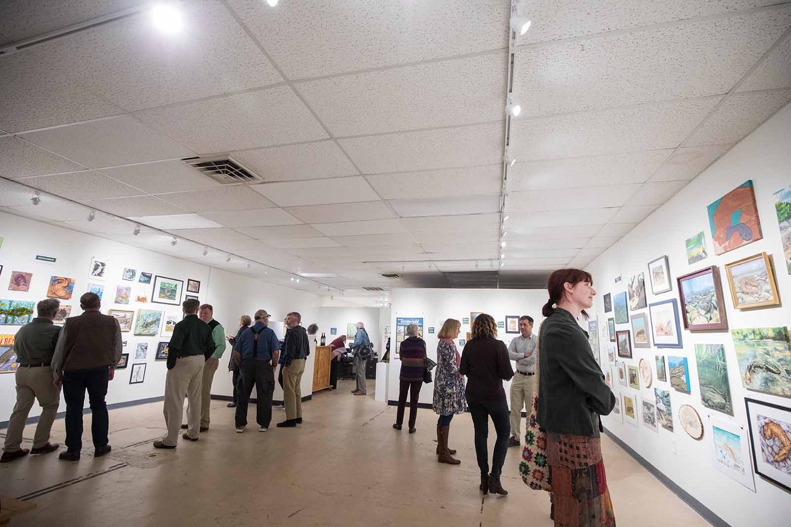 People gathered in an art gallery, looking at various works of art on the wall