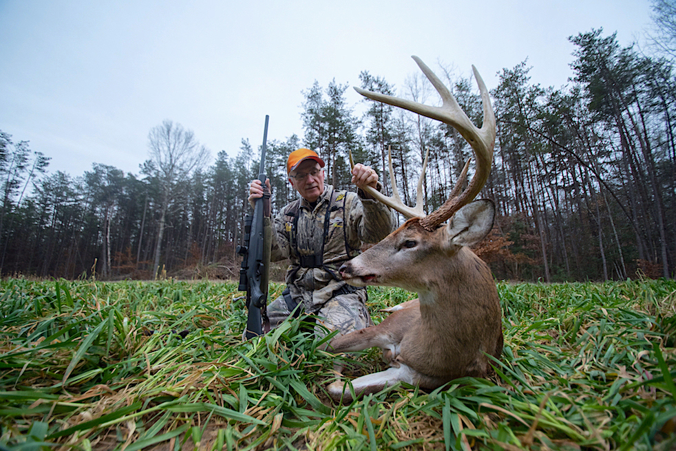 An image of a man with a dead deer he has killed with a rifle
