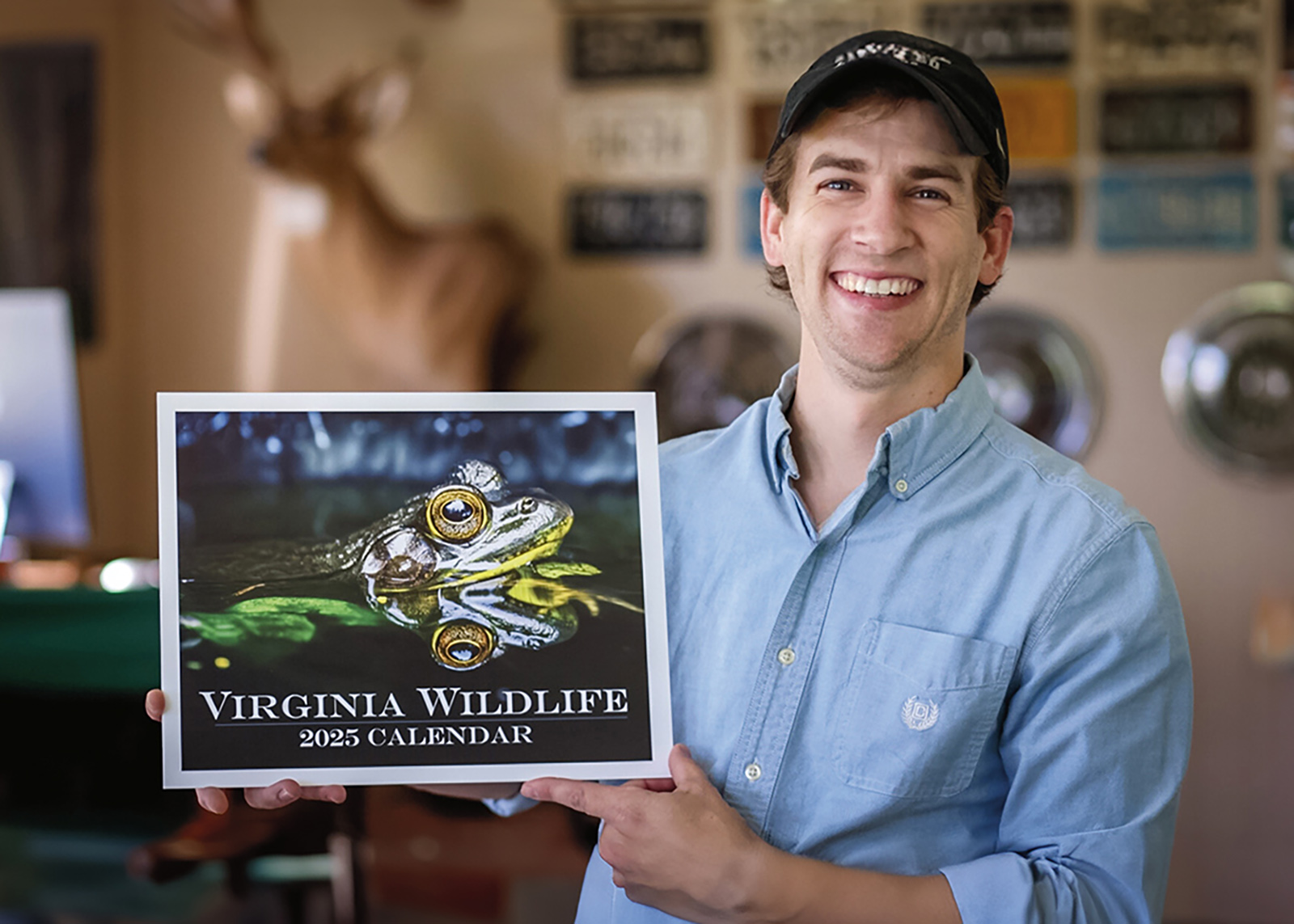 A photo of a man with a wide smile on his face holding a Virginia Wildlife calendar with a large frog photo on the cover.