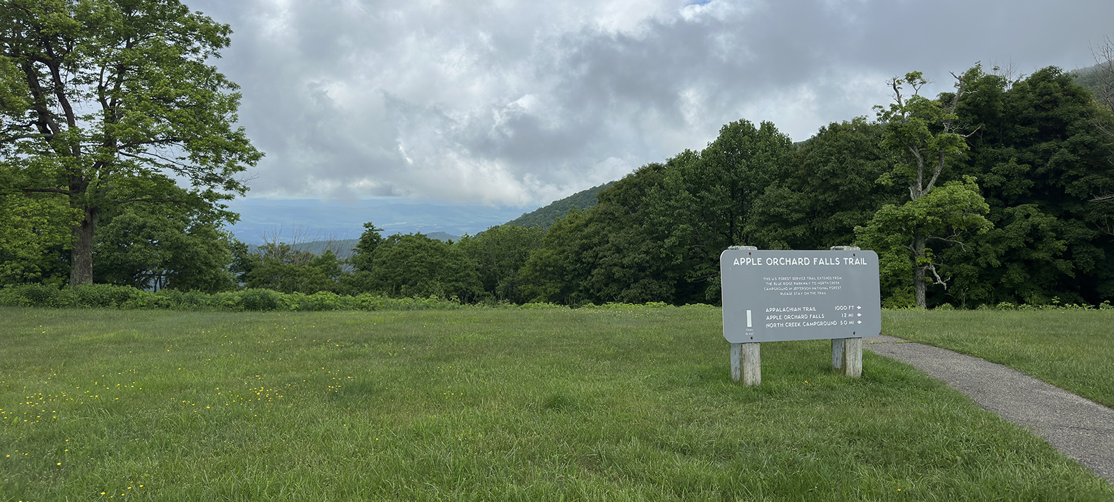 A photo of a green field with a vista and an interpretive sign.