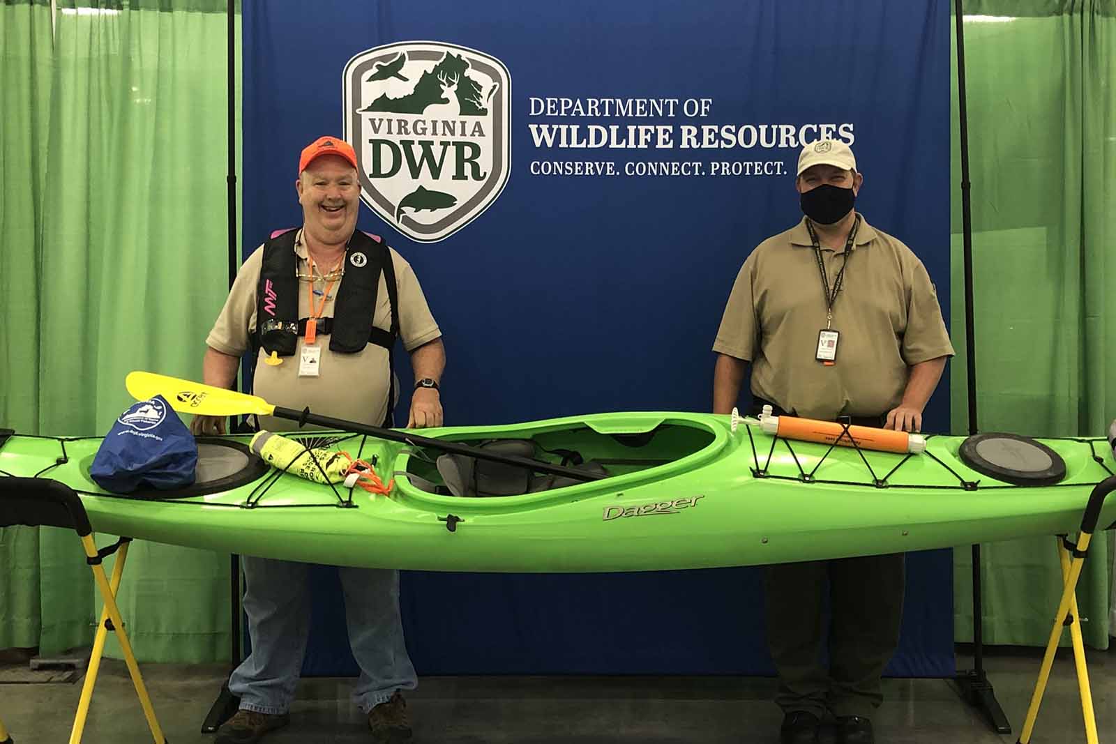Two volunteers standing behind a green kayak