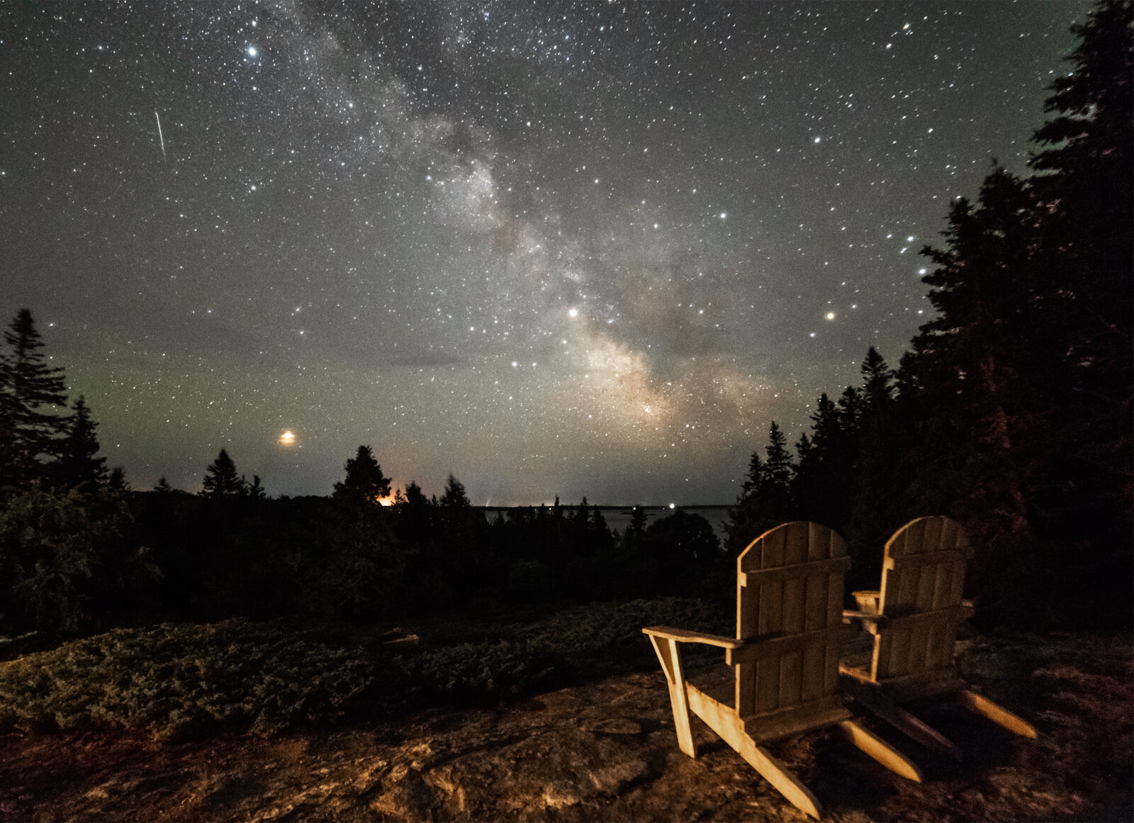 An image of two chairs looking at the swirling galaxy of stars seen in the night sky