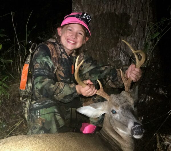 An image of a young girl the the male deer she has killed