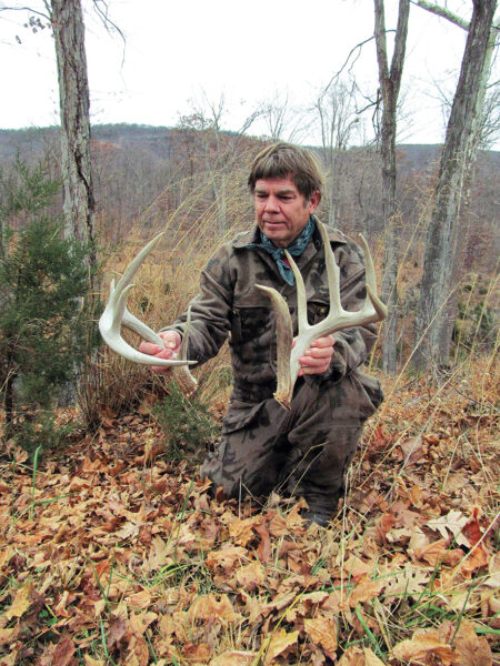 An picture of a man holding two deer antler sheds in a deciduous forest