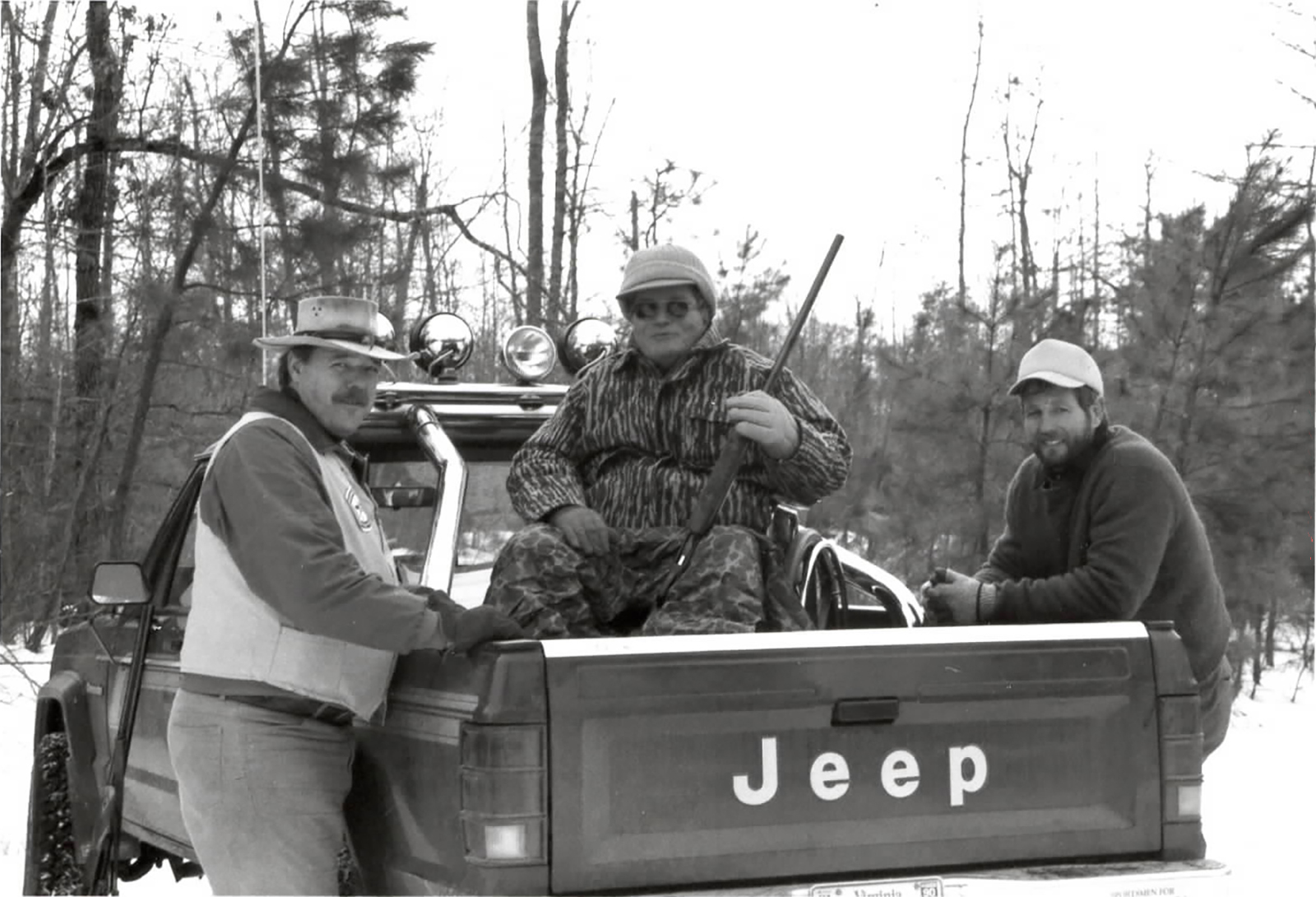 An old black-and-white photo of three deer hunters by a truck.